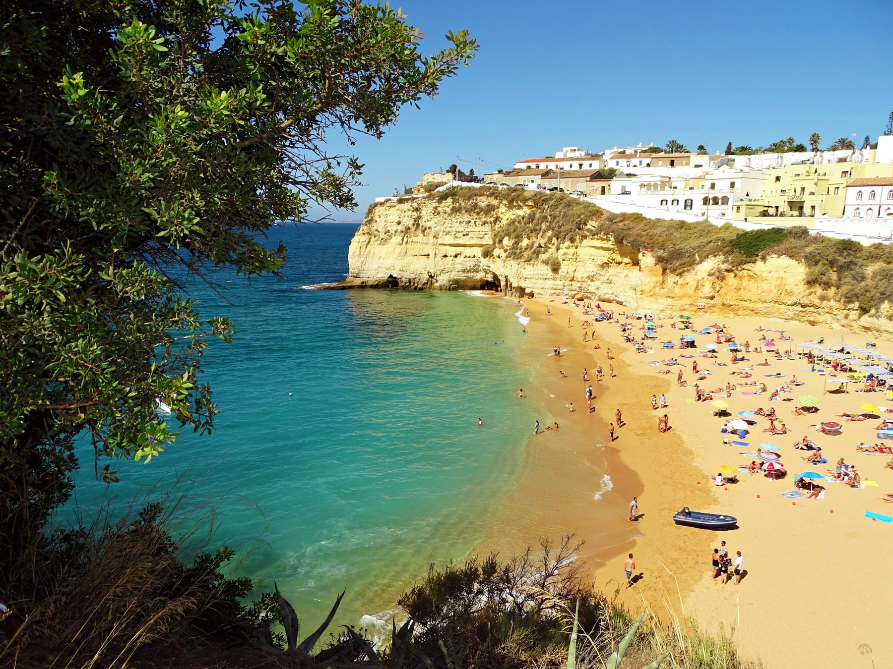 Praia do Carvoeiro: una cala de arena con bañistas y sombrillas bajo las casas blancas del pueblo en el acantilado.